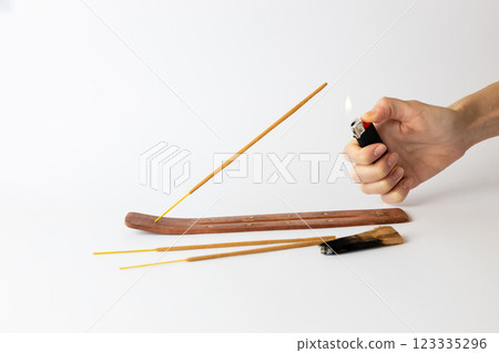 close-up on white background on a long brown stand with stars for incense sticks a new beige palosanto meditation stick is placed a hand with a black lighter setting fire close-up on white background on a long brown stand with stars for incense sticks a new beige palosanto meditation stick is placed a hand with a black lighter setting fire 123335296