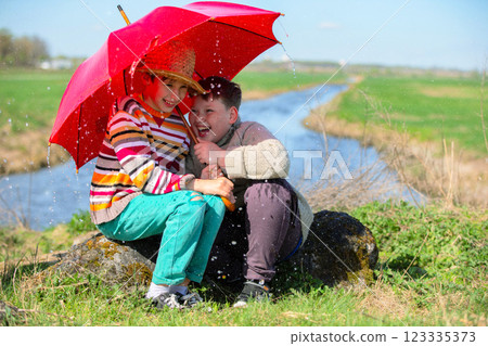 Two boy friends laugh under an umbrella in the rain. Children got caught in the rain outdoors. Two boy friends laugh under an umbrella in the rain. Children got caught in the rain outdoors. 123335373