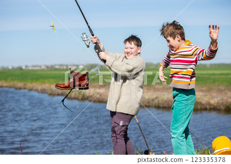Funny fishing. Two of the boy's friends hooked an old shoe with a fishing rod and are laughing. Funny fishing. Two of the boy's friends hooked an old shoe with a fishing rod and are laughing. 123335378