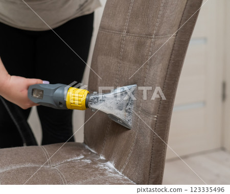 Woman cleaning the back of a fabric chair with a professional washing vacuum cleaner. Woman cleaning the back of a fabric chair with a professional washing vacuum cleaner. 123335496