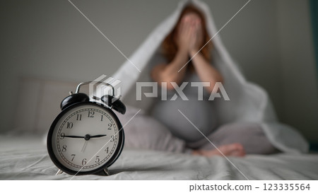 Caucasian pregnant woman sits on the bed and suffers from insomnia. Alarm clock in the foreground.  123335564