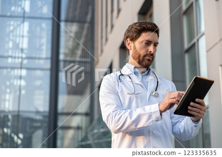 Ginger man in a lab coat with a tablet in hands looking determined 123335635