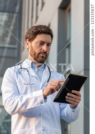 Ginger man in a lab coat with a tablet in hands looking determined 123335637