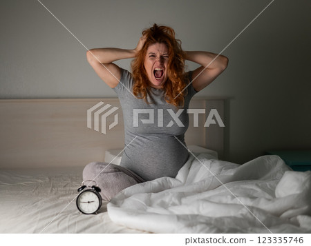 Caucasian pregnant woman sitting in bed and screaming while suffering from insomnia.  123335746