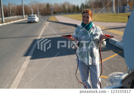 Woman holding clamps for charging a car battery. Woman holding clamps for charging a car battery. 123335817