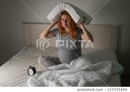 Caucasian pregnant woman sits in bed, holds a pillow on her head and cries. Insomnia. 123335849