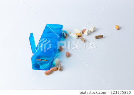white background two bright blue pill boxes with a couple of open lids for taking pills, health care, partial filling, different shapes and colors of pills and vitamins pills lie next to the table 123335850
