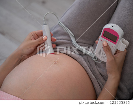 Close-up of a pregnant woman's belly using a home doppler. Blank screen. 123335855