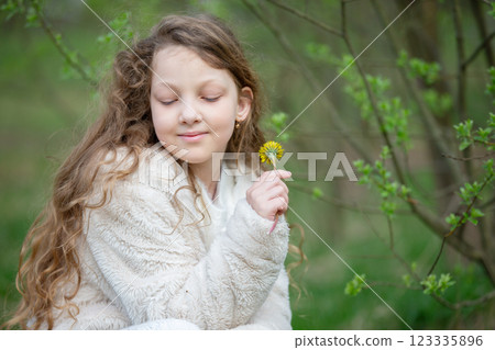 A little blonde girl with a yellow dandelion in a spring park. A little blonde girl with a yellow dandelion in a spring park. 123335896