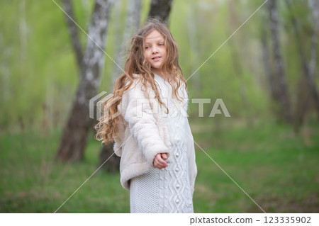 A beautiful girl with long hair in a fur coat poses against the background of a birch grove. 123335902