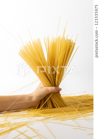 close-up on a white background from the side, a woman's hand with an emphasis on the table holds spaghetti, spilled spaghetti on the table from container, Italian cuisine 123335975