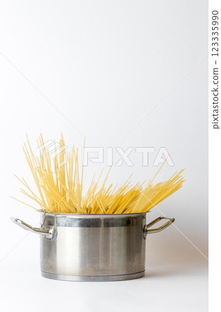 close-up on white background, carefully laid out yellow Italian spaghetti lies in an iron casserole, rules for cooking spaghetti, Italian traditional cuisine close-up on white background, carefully laid out yellow Italian spaghetti lies in an iron casserole, rules for cooking spaghetti, Italian traditional cuisine 123335990
