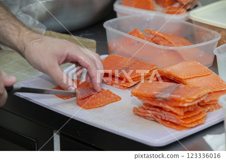 Human hands are slicing red fish with a knife. 123336016