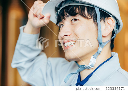 一名戴著頭盔、穿著工作服的年輕人在建築工地工作 123336171