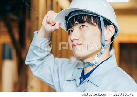 A young man wearing a helmet and work clothes working at a construction site A young man wearing a helmet and work clothes working at a construction site 123336172