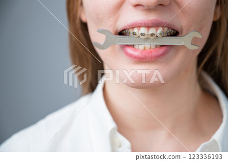 Close-up portrait of a woman with braces holding a wrench in her teeth.  123336193