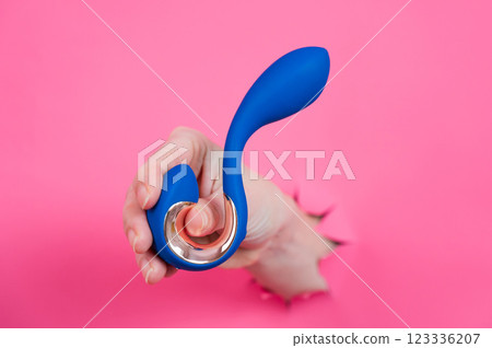Hand with blue vibrator sticking out through pink paper background.  123336207