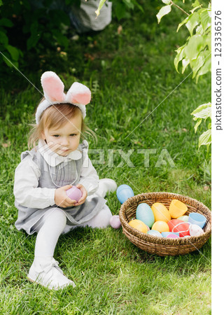 Laughing child at Easter egg hunt baby in pink bunny costume Cute funny girl with Easter eggs and bunny ears at garden. Laughing child at Easter egg hunt baby in pink bunny costume Cute funny girl with Easter eggs and bunny ears at garden. 123336576