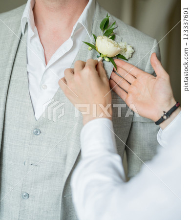 Best man attaches the boutonniere to the lapel of groom jacket. Cropped. Faceless 123337601