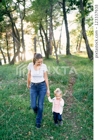 Mom and little girl are walking along the path in the park holding hands Mom and little girl are walking along the path in the park holding hands 123337638