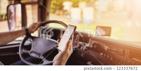 Truck driver sitting behind the wheel and looking at the smartphone. 123337672