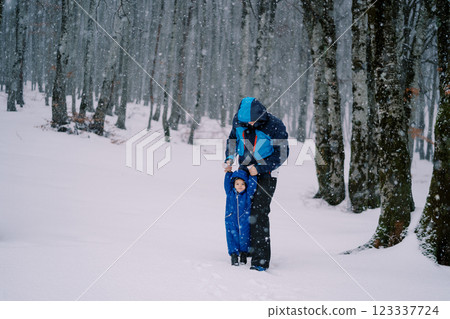 Dad stands with a small child holding hands under a snowfall in the forest 123337724