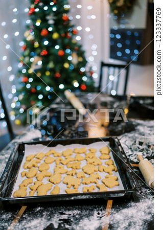 Baked cookies lie on baking paper on a tray on a table near decorated Christmas tree 123337769
