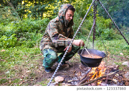 Hunter cooking food in pot over campfire in forest 123337860