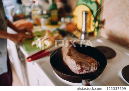 Roast beef is stewed in a pan while the chef cuts vegetables on the table. Cropped 123337899