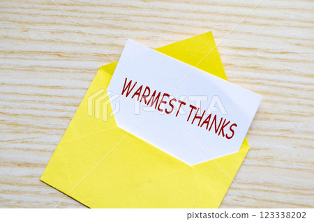 Top view of yellow envelope on a wooden surface with a white card partially pulled out with text Warmest Thanks Top view of yellow envelope on a wooden surface with a white card partially pulled out with text Warmest Thanks 123338202