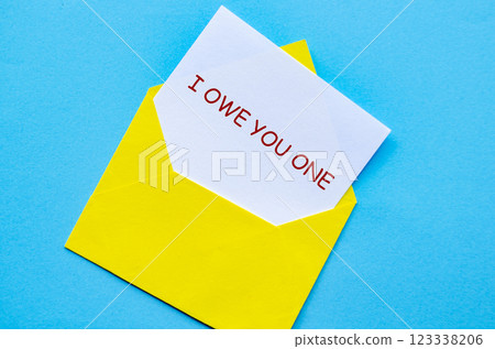 Yellow envelope on a blue cover with a white card partially pulled out with I Owe You One text Yellow envelope on a blue cover with a white card partially pulled out with I Owe You One text 123338206