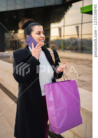 Smiling woman shopping and chatting on her phone outdoors Smiling woman shopping and chatting on her phone outdoors 123338648