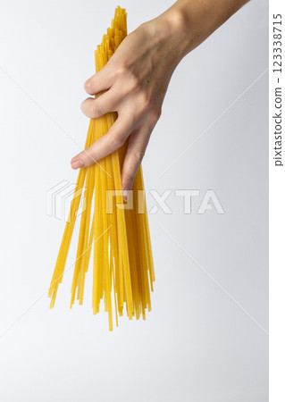 on white background young female thin hand holding durum spaghetti firmly in hands Italian cuisine traditional food bright yellow color spaghetti hand directs spaghetti from top to bottom on white background young female thin hand holding durum spaghetti firmly in hands Italian cuisine traditional food bright yellow color spaghetti hand directs spaghetti from top to bottom 123338715