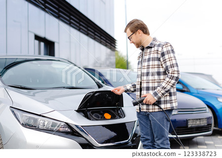 Young man plugging charging cable into the car socket. Electric car charging concept 123338723