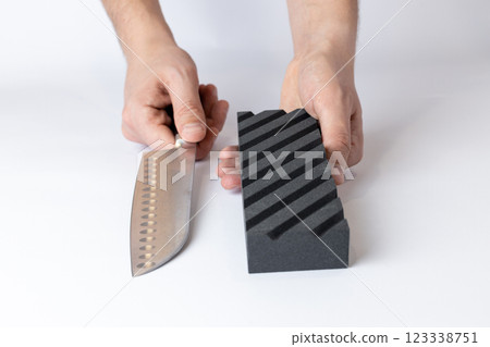 closeup on a white background on a table in a man's hands lies straight a large knife for sharpening and a black corrugated sharpening stone for the first sharpening closeup on a white background on a table in a man's hands lies straight a large knife for sharpening and a black corrugated sharpening stone for the first sharpening 123338751