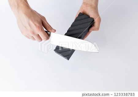 top shot on white background on a table, man hands sharpen a steel knife protection against cuts, a black medium-hard stone for sharpening knives professional knife for slicing vegetables top shot on white background on a table, man hands sharpen a steel knife protection against cuts, a black medium-hard stone for sharpening knives professional knife for slicing vegetables 123338783