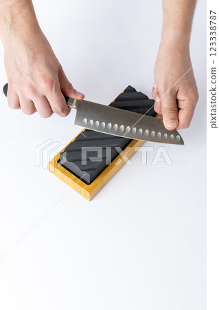 close up on white background on a table, man hands sharpen a steel knife protection against cuts, a black medium-hard stone for sharpening knives professional knife for slicing vegetables 123338787