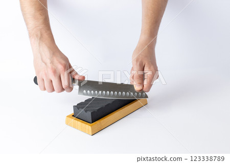 on white background on a table, man hands sharpen a steel knife protection against cuts, a black medium-hard stone for sharpening knives professional knife for slicing vegetables 123338789