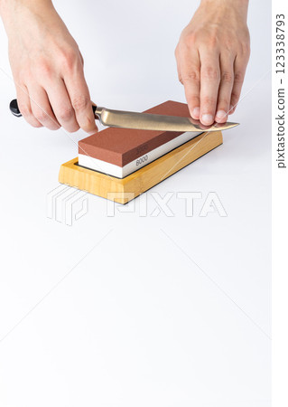 close up on white background on a table, man hands sharpen a steel knife protection against cuts, a red medium-hard stone for sharpening knives 123338793