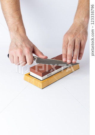 close up on white background on a table, man hands sharpen a steel knife protection against cuts, a red medium-hard stone for sharpening knives close up on white background on a table, man hands sharpen a steel knife protection against cuts, a red medium-hard stone for sharpening knives 123338796