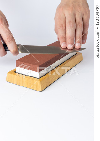 close up on white background on a table, man hands sharpen a steel knife protection against cuts, a red medium-hard stone for sharpening knives close up on white background on a table, man hands sharpen a steel knife protection against cuts, a red medium-hard stone for sharpening knives 123338797