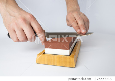close up on white background on a table, man hands sharpen a steel knife protection against cuts, a red medium-hard stone for sharpening knives 123338800