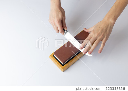 on white background on a table, women's hands sharpen a steel knife, a lock under the arm, protection against cuts, a red medium-hard stone for sharpening knives 123338836