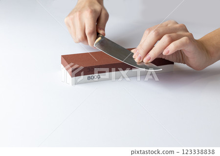 on white background on a table, women's hands sharpen a steel knife, a lock under the arm, protection against cuts, a red medium-hard stone for sharpening knives 123338838