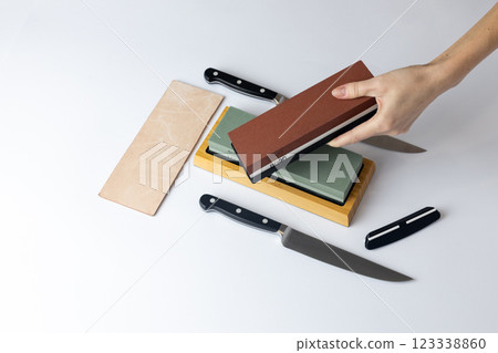 on white background on the counter lies the entire set of equipment for sharpening and polishing kitchen knives, the girl s hands hold a red stone of medium hardness, knives on the table on white background on the counter lies the entire set of equipment for sharpening and polishing kitchen knives, the girl s hands hold a red stone of medium hardness, knives on the table 123338860