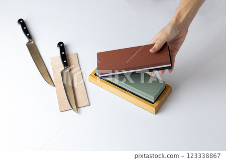 on white background on the counter lies the entire set of equipment for sharpening and polishing kitchen knives, the girl s hands hold a red stone of medium hardness, knives on the table 123338867