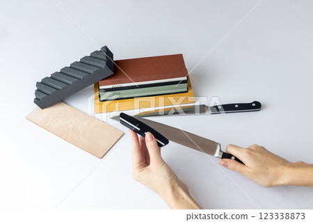 white background on counter lies all the equipment - a set for sharpening and polishing kitchen knives - the girl's hands are fixing the fuse and the locking device for knife protection against cuts 123338873