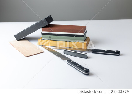 white background on stand lies all the equipment a set for sharpening and polishing kitchen knives and various blades different abrasiveness of stones a retainer for knives sheet tanned leather knives 123338879