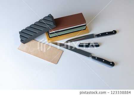 white background on stand lies all the equipment a set for sharpening and polishing kitchen knives and various blades different abrasiveness of stones a retainer for knives sheet tanned leather knives white background on stand lies all the equipment a set for sharpening and polishing kitchen knives and various blades different abrasiveness of stones a retainer for knives sheet tanned leather knives 123338884