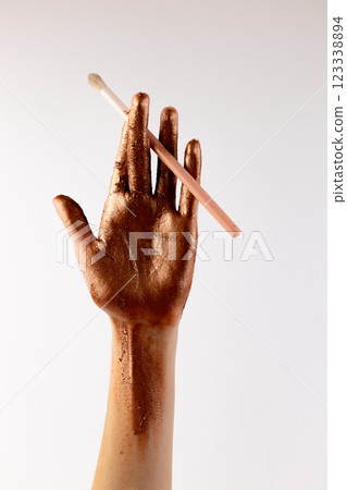 A Beautifully Artistic Gesture with a Hand Coated in Shimmering Bronze and Holding a Makeup Brush Against a Minimalist Background for a Stunning Visual Effect A Beautifully Artistic Gesture with a Hand Coated in Shimmering Bronze and Holding a Makeup Brush Against a Minimalist Background for a Stunning Visual Effect 123338894